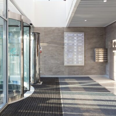 Bright office lobby with glass revolving doors, wall-mounted directory, and mailboxes.
