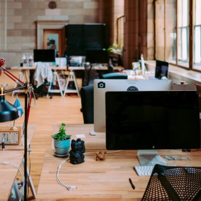 Open-plan office with desks, iMacs, desk lamps, and natural light from large windows.