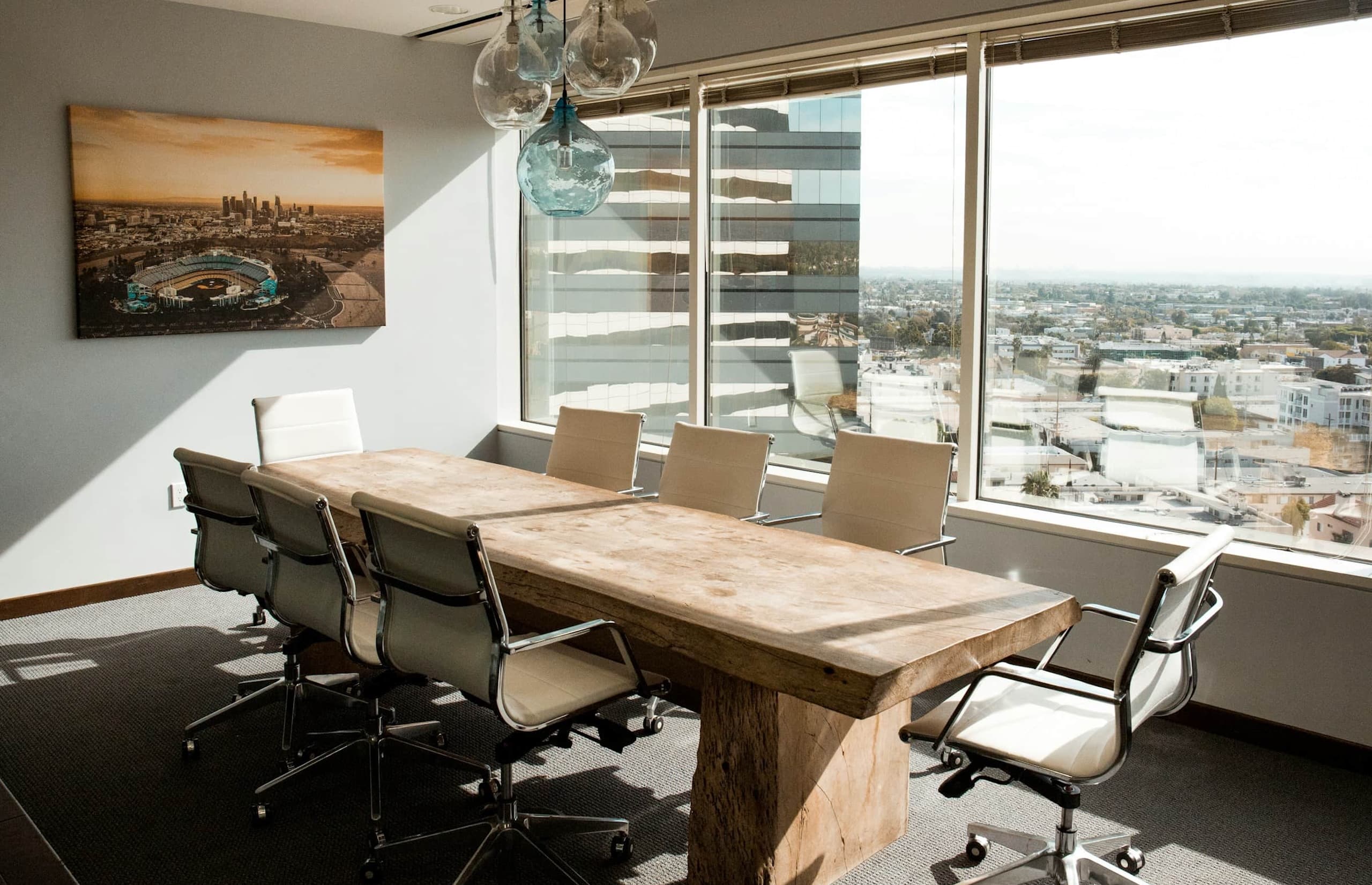 Skedda Software Review: The Good, the Gaps, the Price Empty meeting room with a large wooden table, white office chairs, and floor-to-ceiling windows overlooking a cityscape.