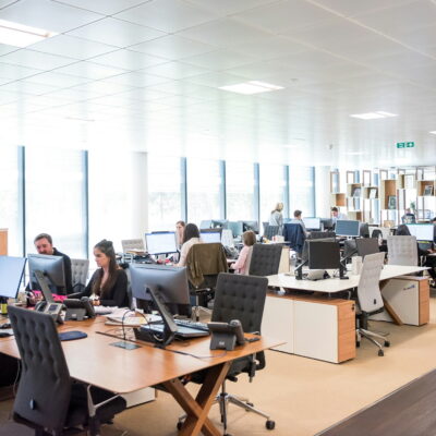 Modern open-plan office with employees working at desks and computer monitors.