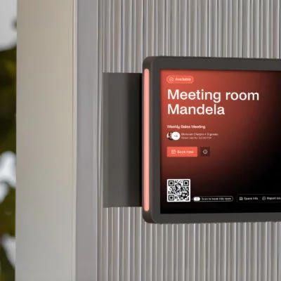 Wall-mounted meeting room display running Archie Rooms app, showing availability, schedule, and a QR code for room booking.