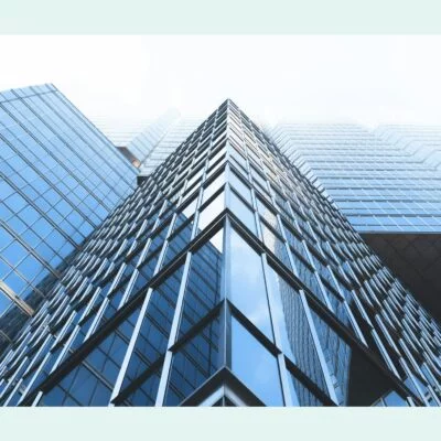 Low-angle view of a modern glass skyscraper with reflective windows and sharp architectural lines against a bright sky.