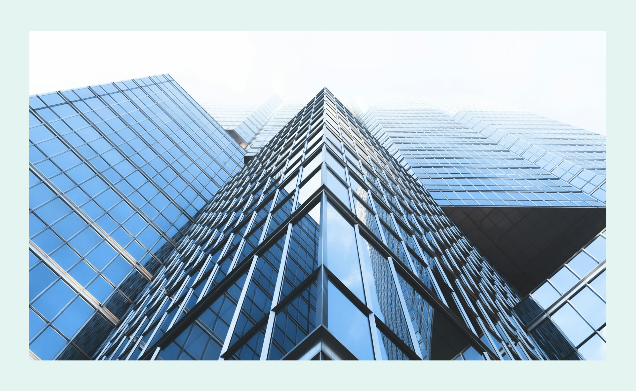 Low-angle view of a modern glass skyscraper with reflective windows and sharp architectural lines against a bright sky.