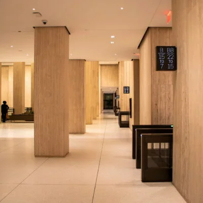 Modern office building lobby with light stone walls, security turnstiles, and digital floor directories.