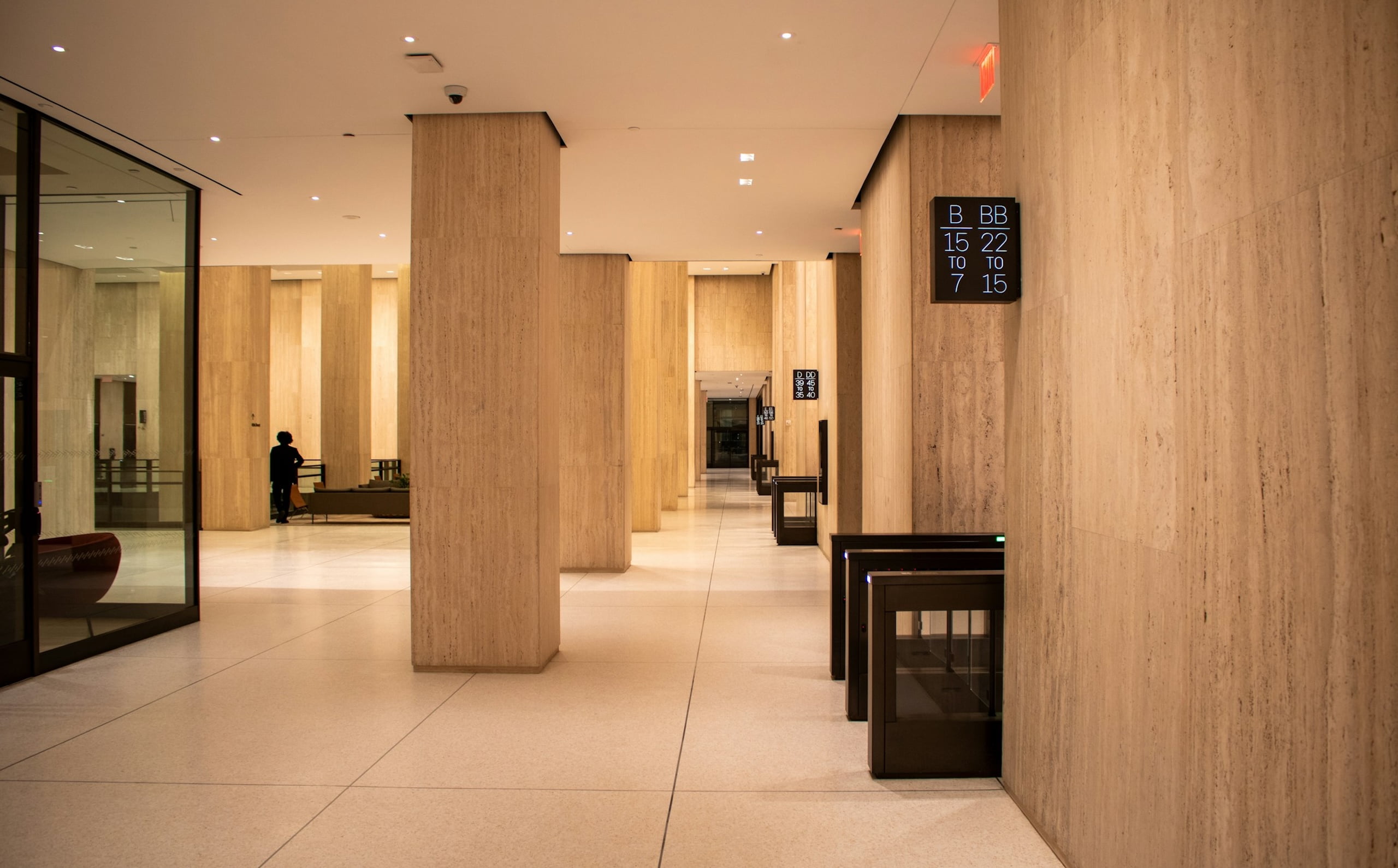 Modern office building lobby with light stone walls, security turnstiles, and digital floor directories.