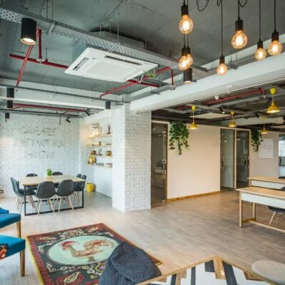 Modern open coworking area with hanging lights, colorful chairs and large tables.