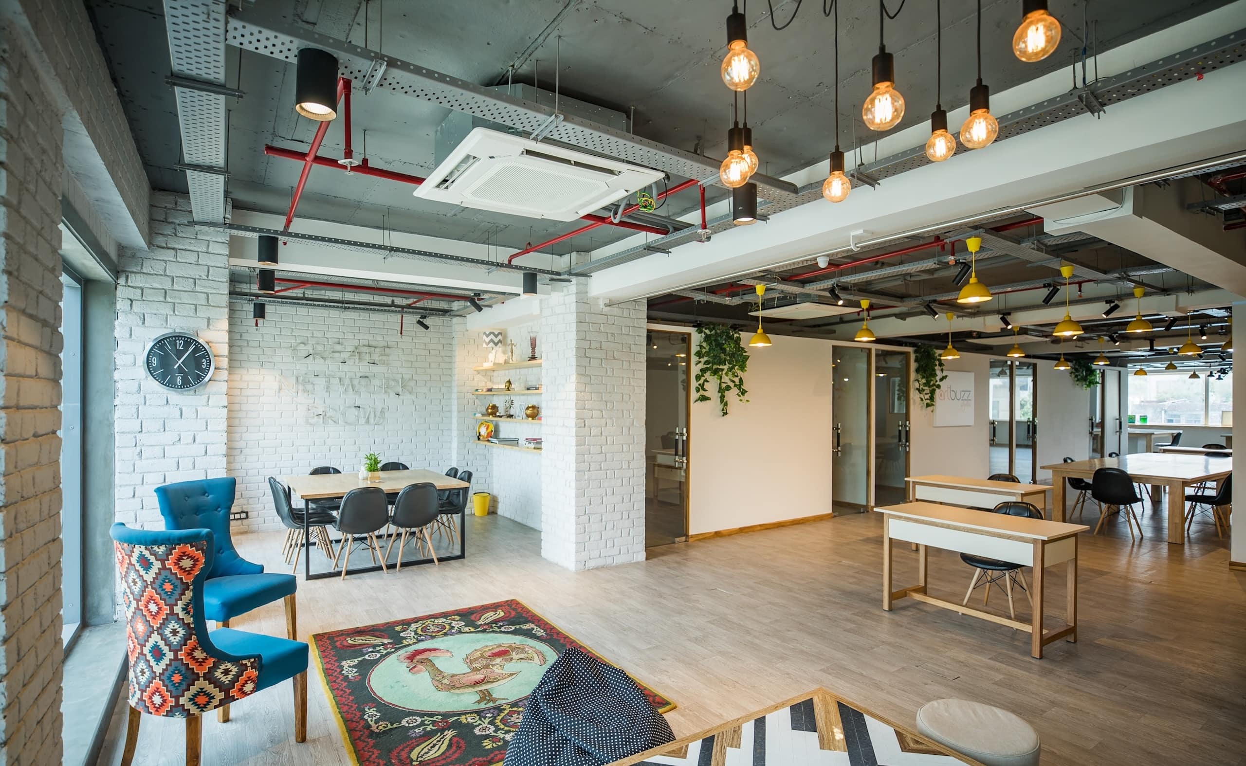 Modern open coworking area with hanging lights, colorful chairs and large tables.
