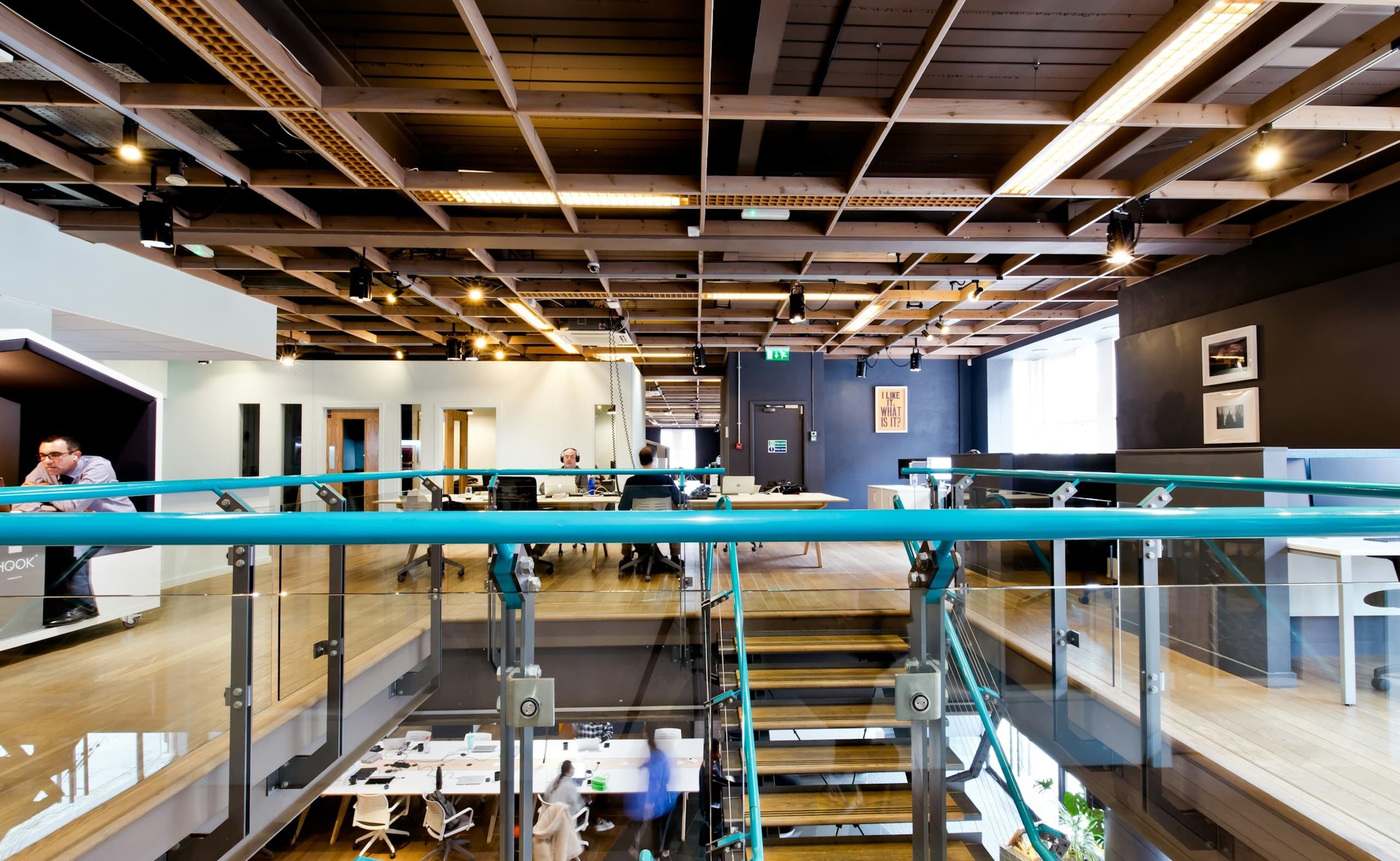 Optix Coworking Software Alternatives: Features & Pricing Spacious coworking area with desks on two levels, connected by stairs with blue handrails.