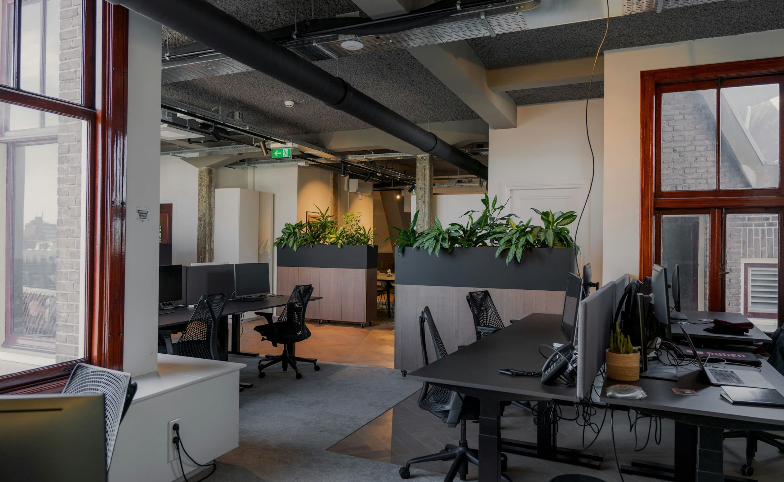 Modern open-plan office with black desks, computer monitors, and planters dividing the workspace.