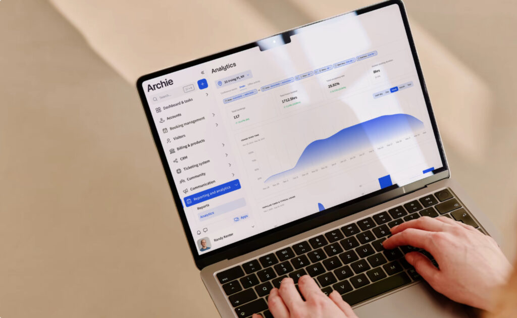 Close-up of a person using a laptop with the Archie coworking software dashboard open, showing analytics and space usage charts.