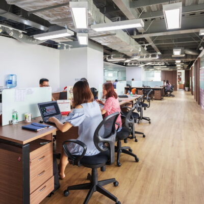 Open-plan office with employees working at rows of desks, featuring modern lighting and a clean, spacious layout.