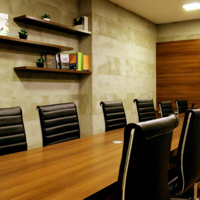 Modern conference room with a long wooden table, black chairs, bookshelves, and a wall-mounted TV.