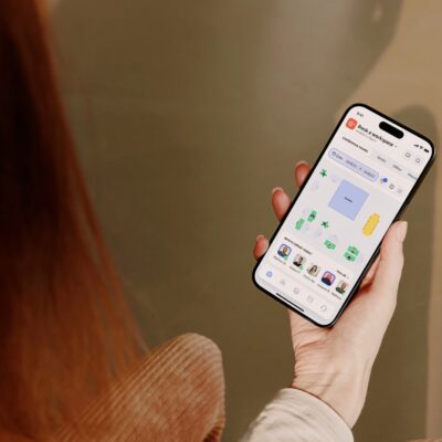 Person holding a smartphone using Archie, workspace booking app, with an interactive floor plan and coworker seating visibility.