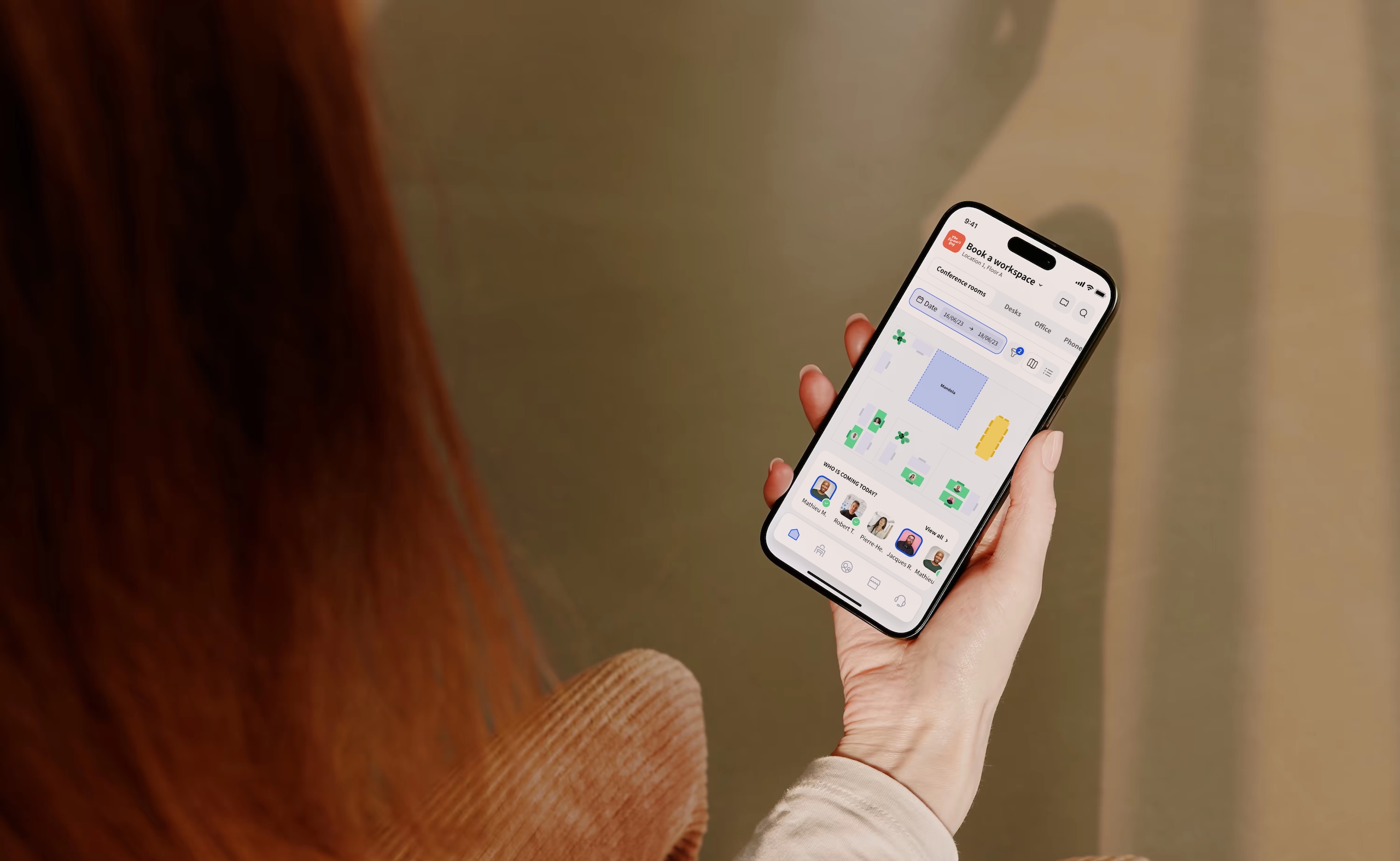 Person holding a smartphone using Archie, workspace booking app, with an interactive floor plan and coworker seating visibility.