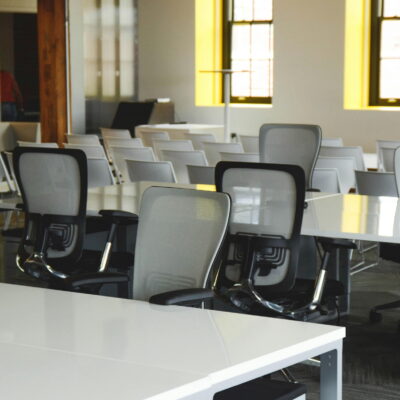 Bright coworking space with white desks, ergonomic chairs, and natural light coming through large windows.