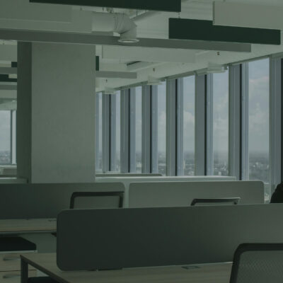 Quiet open office with desk dividers and a person sitting by large windows overlooking the city.