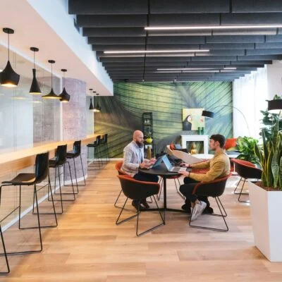 Modern coworking space with shared seating, high tables, and people working together on laptops.