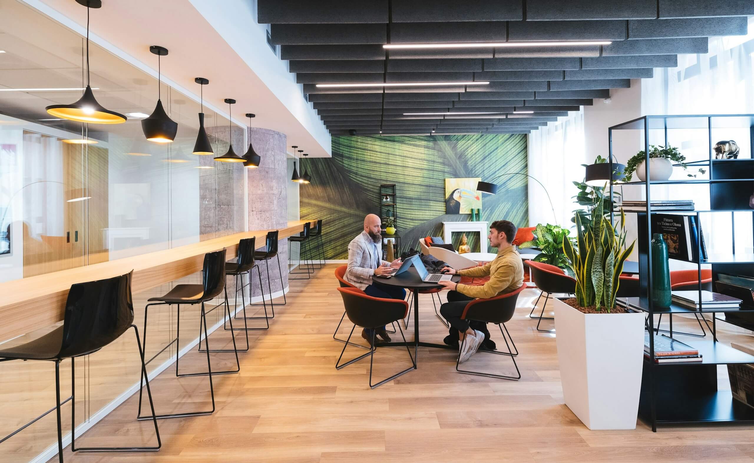 Modern coworking space with shared seating, high tables, and people working together on laptops.