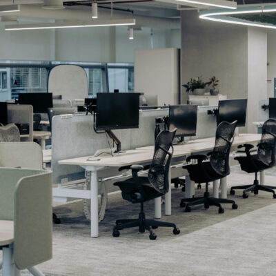 Open office with rows of desks, computer monitors, and ergonomic chairs in a modern workspace.