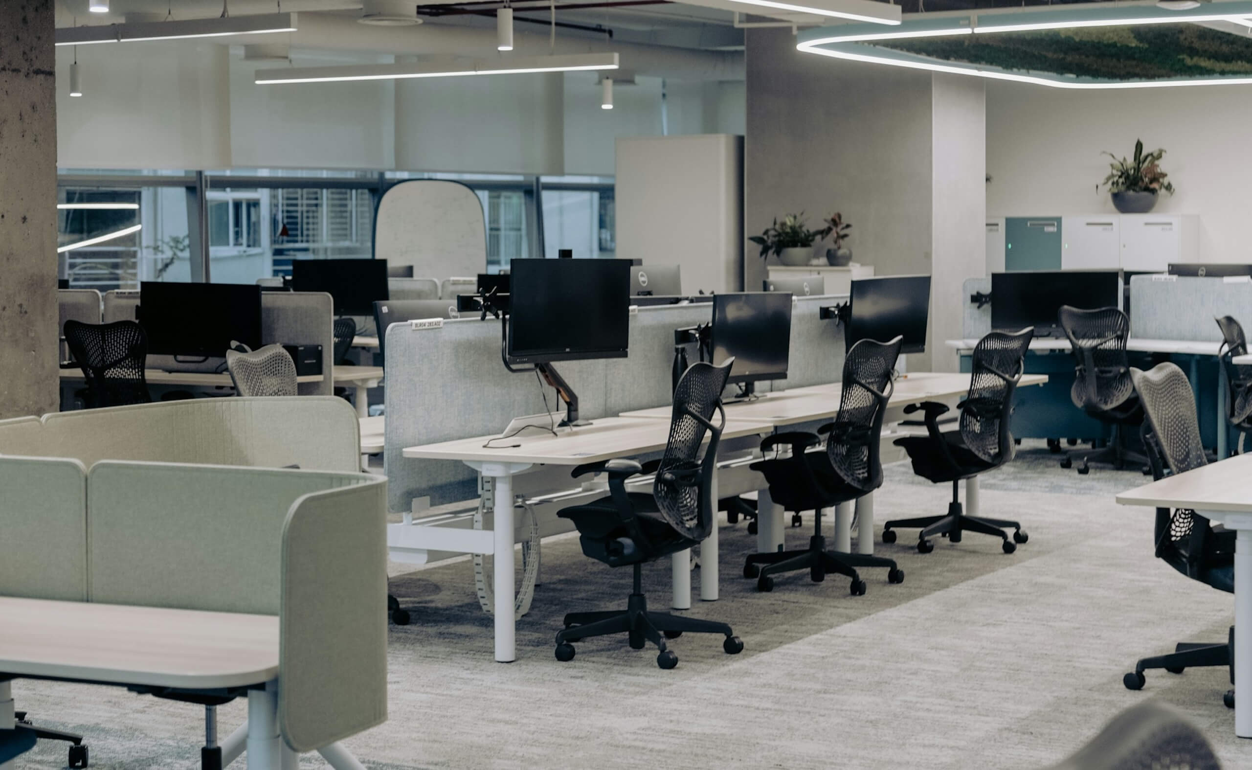 Open office with rows of desks, computer monitors, and ergonomic chairs in a modern workspace.