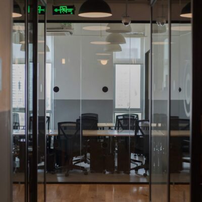 Glass meeting room inside a modern office with shared desks and chairs visible through the glass walls.