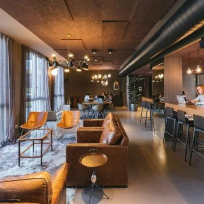 Modern coworking space with lounge seating, shared tables, and people working on laptops.