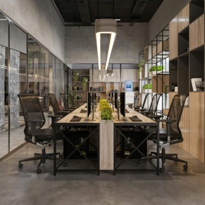 Modern office workspace with shared desks, computer monitors, and glass meeting rooms.