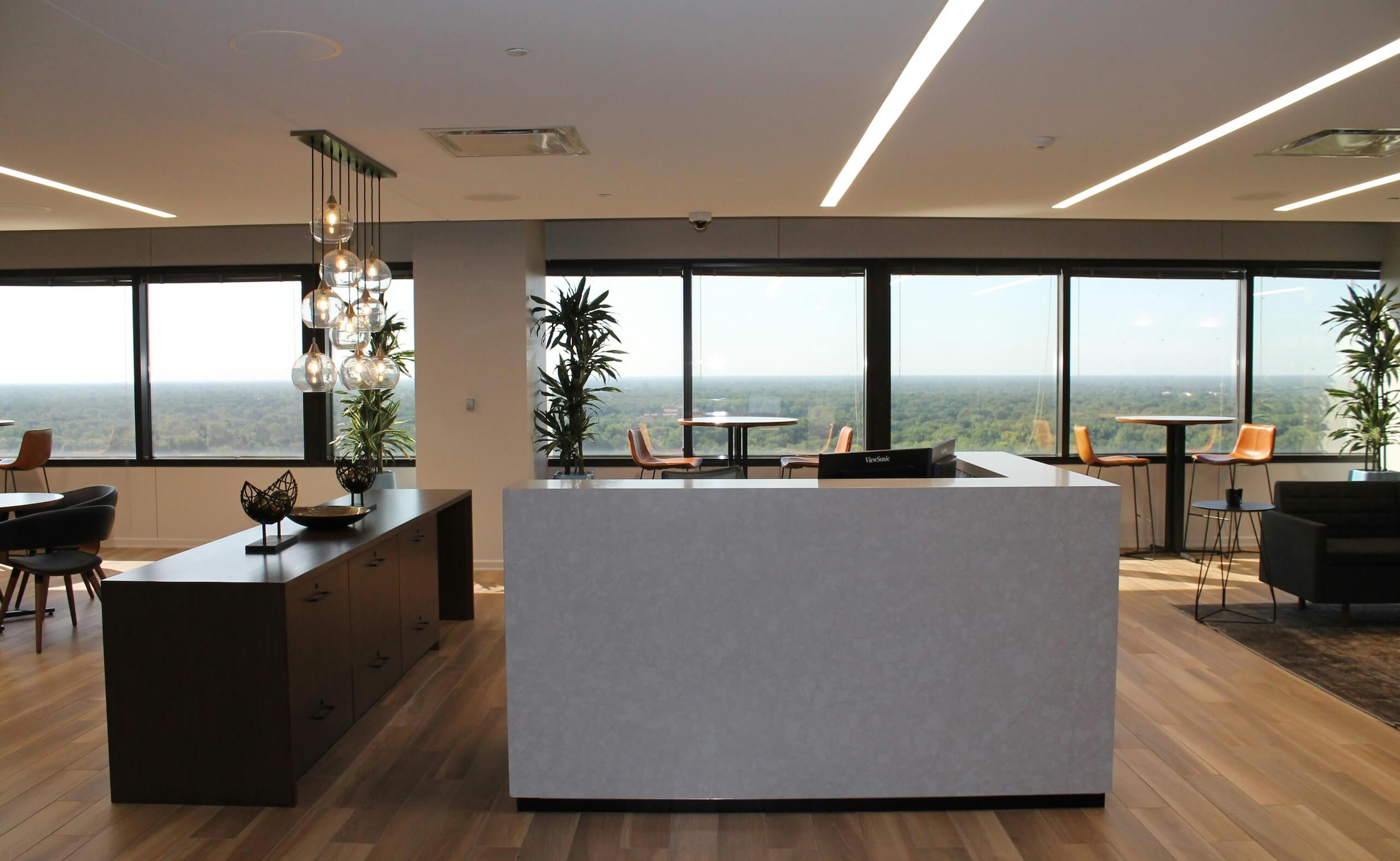 Modern office reception area with front desk, seating, and large windows overlooking the city.