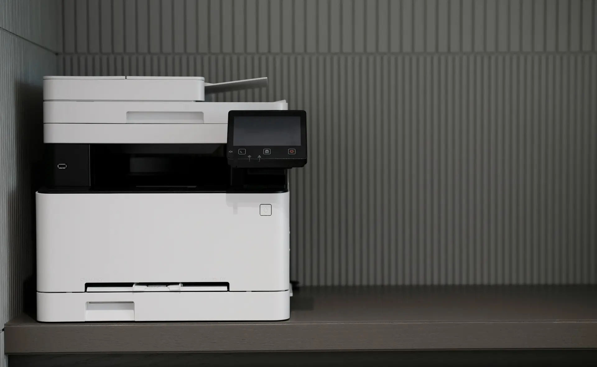Office printer on a cabinet against a dark textured wall.